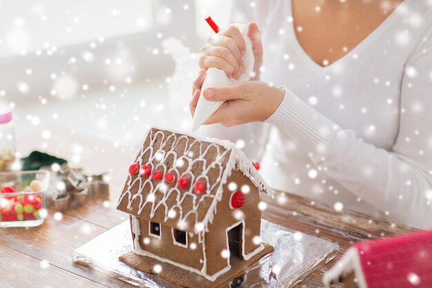 concepto de cocina, gente, navidad y decoración - cerca de una mujer feliz haciendo casas de pan de jengibre en casa