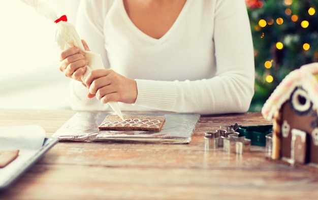 concepto de cocina, gente, navidad y decoración - cerca de una mujer feliz haciendo casas de pan de jengibre en casa