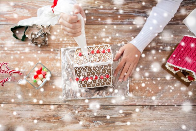 concepto de cocina, gente, navidad y decoración - cerca de una mujer feliz haciendo casas de pan de jengibre en casa