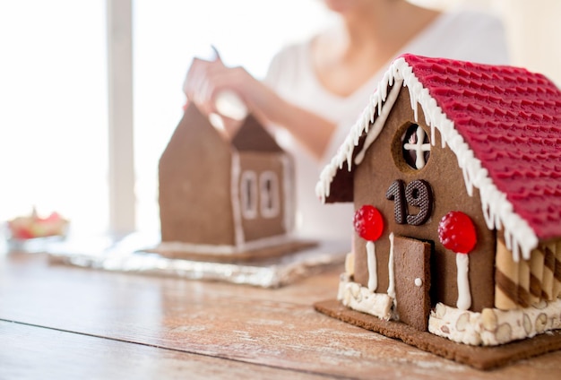 Foto concepto de cocina, gente, navidad y decoración - mujer feliz haciendo casas de pan de jengibre en casa