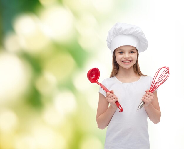 concepto de cocina y gente - niña sonriente con sombrero de cocinero con cucharón y batidor