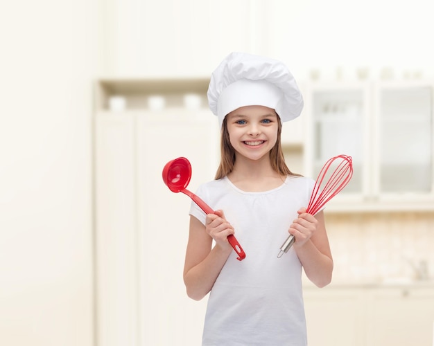 concepto de cocina y gente - niña sonriente con sombrero de cocinero con cucharón y batidor