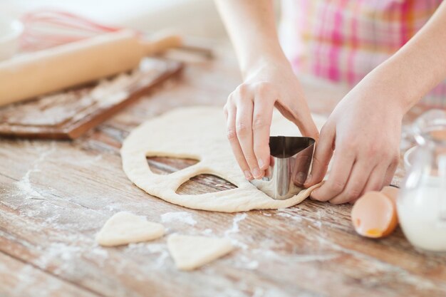 concepto de cocina y hogar - cierre de manos femeninas haciendo galletas de masa fresca en casa