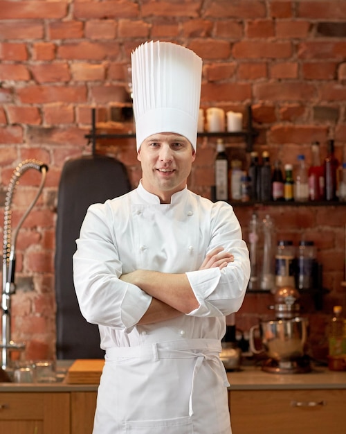 concepto de cocina y personas - cocinero de chef masculino feliz con las manos cruzadas en la cocina del restaurante