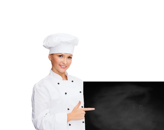 concepto de cocina, publicidad y personas - chef sonriente, cocinera o panadera señalando con el dedo a la pizarra en blanco sobre fondo blanco