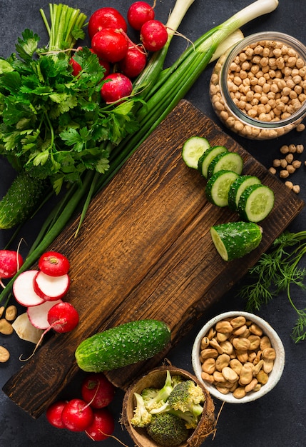 Concepto de cocina vegetariana comida vegetariana saludable. Tabla de cocina de corte de madera con verduras frescas, hierbas y cereales en la vista superior de fondo oscuro