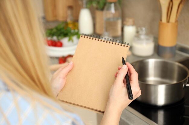 El concepto de cocinar con una mujer tiene un cuaderno y un bolígrafo en blanco