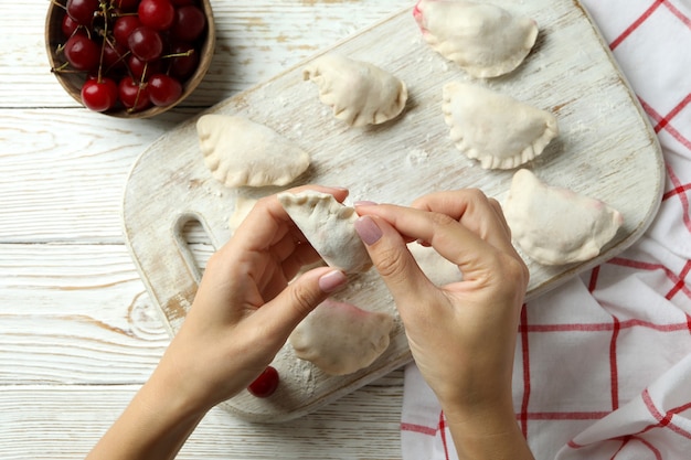 Concepto de cocinar pierogi con cereza sobre mesa de madera blanca