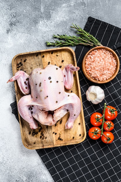 Concepto de cocinar pollo entero. Ingredientes romero, sal rosa, ajo y tomates cherry. Fondo gris Vista superior. Espacio para texto