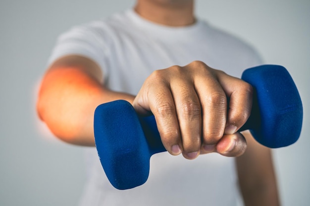 Concepto de codo de tenista El hombre usa una mancuerna azul para la fisioterapia El área de síntomas del dolor se muestra en color rojo Conocimiento de la atención médica Primer plano medio