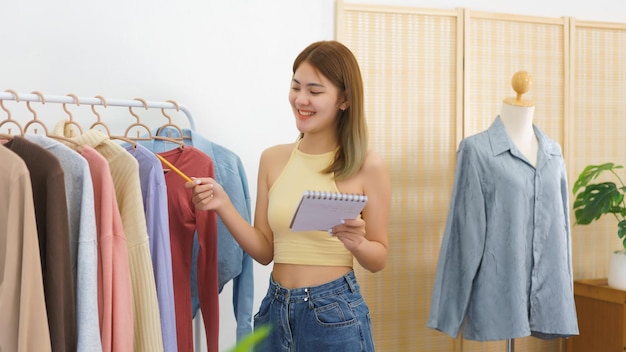 Concepto de comerciante en línea Diseñador de moda revisando ropa de stock para pedidos en línea en la oficina en casa