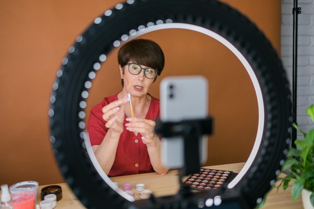 Concepto de comercio electrónico y blogs de belleza y cosméticos Maquilladora femenina madura profesional probando nuevos cosméticos grabando revisión de video sobre productos cosméticos en casa