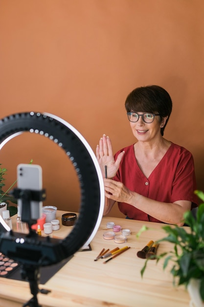 Concepto de comercio electrónico y blogs de belleza y cosméticos Maquilladora femenina madura profesional probando nuevos cosméticos grabando revisión de video sobre productos cosméticos en casa