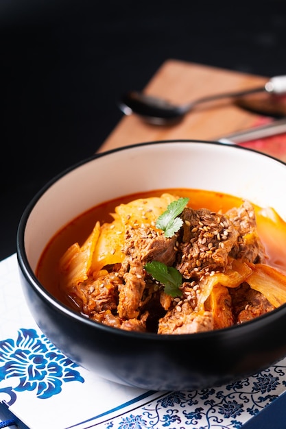 Concepto de comida asiática Carne de res picante y sopa Kimchi o estofado Kimchi Jjigae en tazón de cerámica negra sobre tabla de madera con espacio para copiar