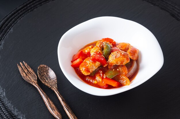 Concepto de comida asiática pollo agridulce en plato de cerámica blanca sobre fondo de piedra pizarra negra