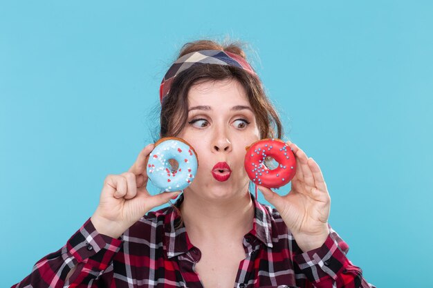 Concepto de comida chatarra, dieta y estilo de vida poco saludable - mujer pin-up con rosquillas sobre el fondo azul.