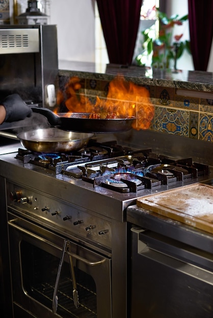 Concepto de comida El chef fríe en una sartén los tomates y las ostras preparando un plato una sartén cubierta de llamas El proceso de cocinar espaguetis con mariscos