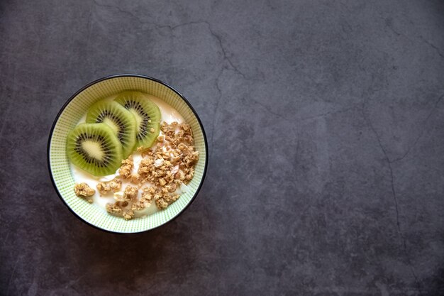 Concepto de comida de cocción Delicioso postre de yogur griego, kiwi y granola en un recipiente sobre un fondo oscuro