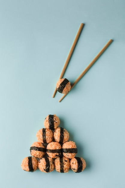 Concepto de comida coreana: bolas de arroz con semillas de sésamo y algas nori, servidas con salsa de soja, palillos sobre un fondo azul brillante. Vista superior con espacio de copia. Orientación vertical.