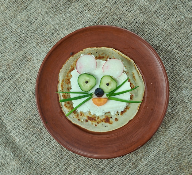 Foto concepto de comida creativa de gato hecho de panqueques, brynza, pepino y aceitunas. menú infantil