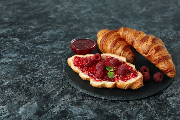 Concepto de comida deliciosa con croissants con mermelada de frambuesa sobre fondo negro ahumado