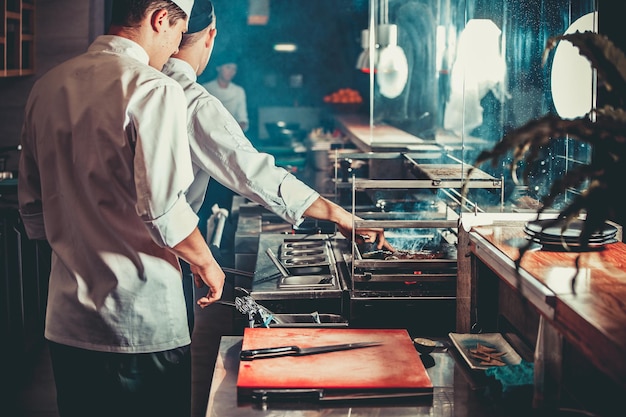 Concepto de comida dos chefs en uniforme blanco supervisan el grado de asar la carne con la mano en el interior de