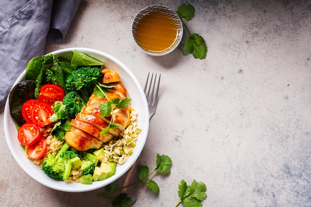 Concepto de comida equilibrada. Ensalada de pollo, brócoli y quinua en un tazón blanco, fondo gris, vista superior.