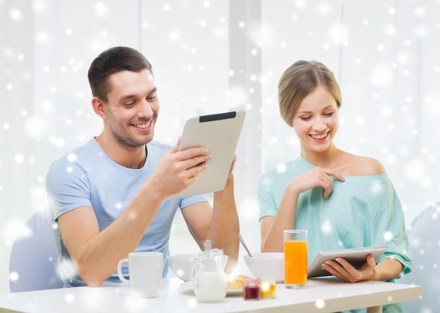 concepto de comida, familia, personas y tecnología - pareja sonriente con computadoras tablet pc leyendo noticias y desayunando en casa