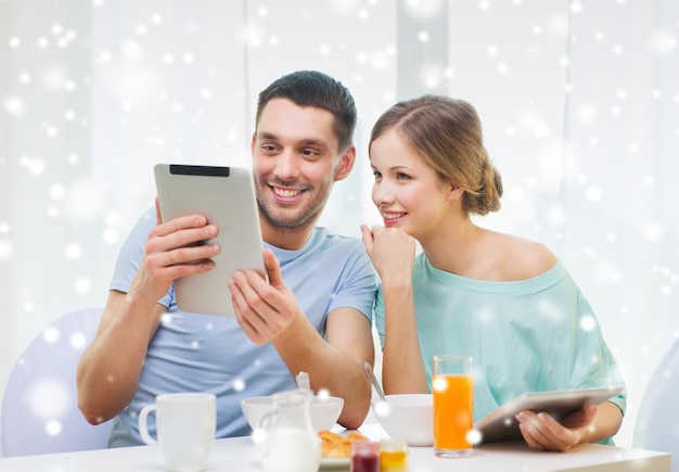 concepto de comida, familia, personas y tecnología - pareja sonriente con computadoras tablet pc leyendo noticias y desayunando en casa