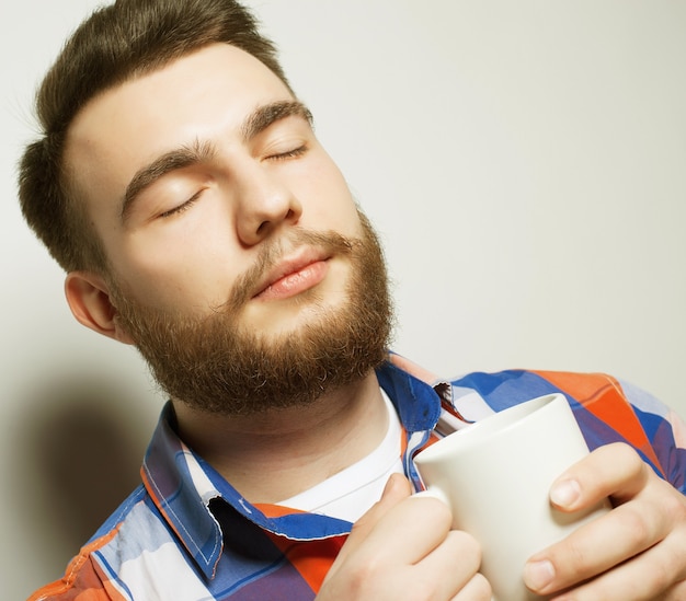 Concepto de comida, felicidad y personas: joven barbudo con una taza de café sobre fondo gris