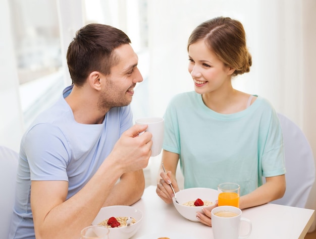 concepto de comida, hogar, pareja y felicidad - pareja sonriente desayunando en casa