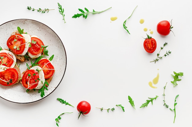 Concepto de comida italiana. Abra los emparedados con la mozzarella, los tomates y la rúcula en la placa blanca. Sobrecarga, composición del marco