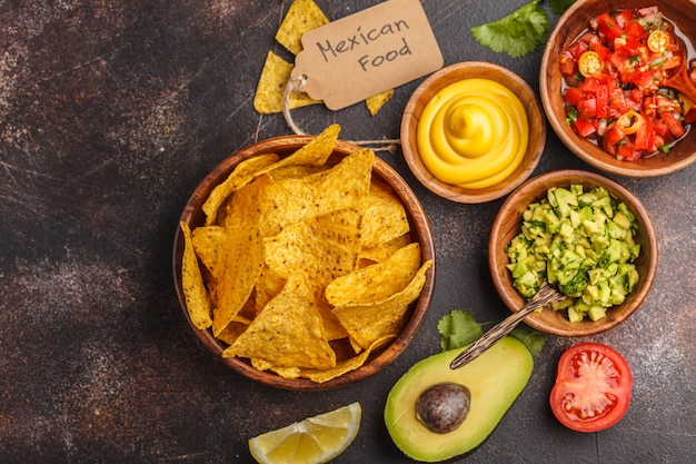 Concepto de comida mexicana. Nachos: chips de totopos de maíz amarillo con varias salsas en cuencos de madera: guacamole, salsa de queso, pico del gallo, espacio de copia, vista superior