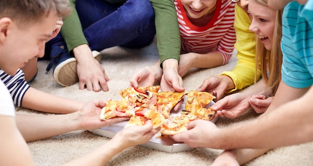 concepto de comida, ocio y amistad - cerca de amigos adolescentes felices comiendo pizza en casa