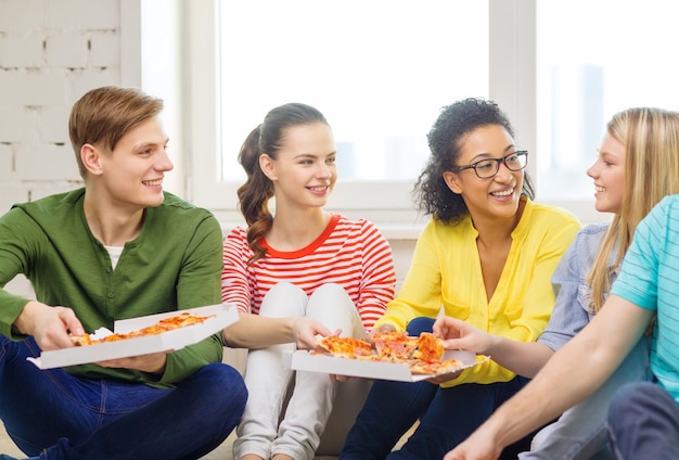 concepto de comida, ocio y felicidad - cinco adolescentes sonrientes comiendo pizza en casa