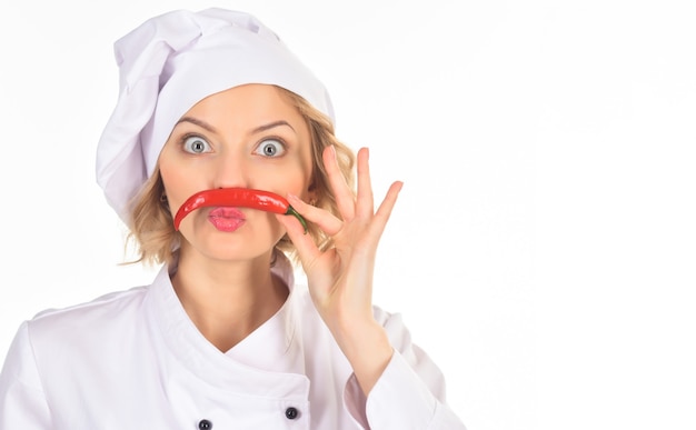 Concepto de comida picante - chef mujer haciendo bigote de ají candente. Cocinero profesional en traje blanco sostiene ají candente como bigote mientras mira a la cámara con los ojos muy abiertos. Copie el espacio.