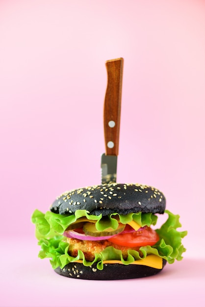 Concepto de comida rápida. Hamburguesa negra jugosa con el cuchillo en fondo rosado. Comida para llevar. Marco de dieta poco saludable con espacio de copia