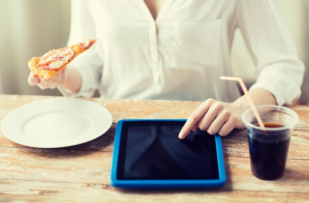 Foto concepto de comida rápida, personas, tecnología y dieta - cierre de manos de mujer con computadora de tablet pc, pizza y coca cola contando calorías en la mesa