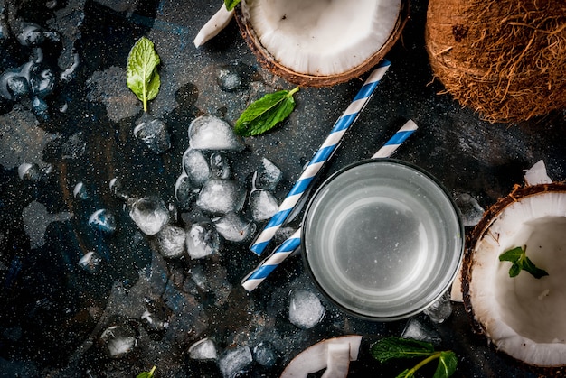 Concepto de comida saludable. Agua de coco orgánico fresco con cocos, cubitos de hielo y menta, en azul oscuro oxidado, vista superior de copyspace