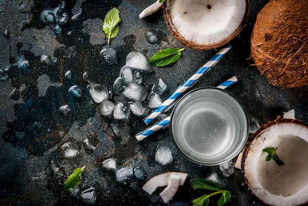 Concepto de comida saludable. Agua de coco orgánico fresco con cubitos de hielo de coco y menta sobre fondo azul oxidado vista superior