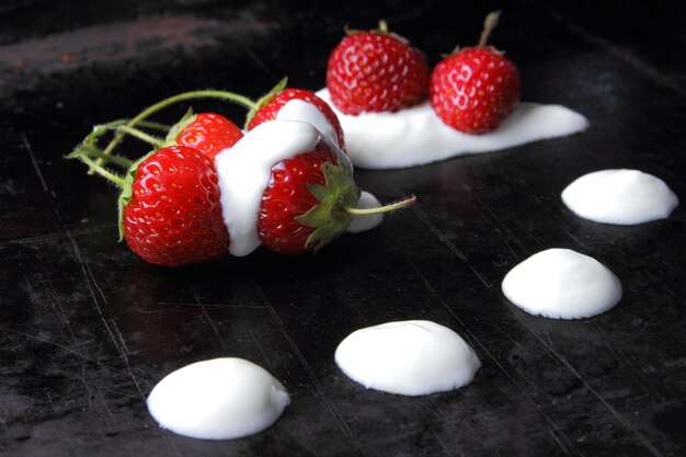 Concepto de comida saludable Fresas dulces jugosas rojas con crema sobre un fondo negro Primer plano de bayas rojas