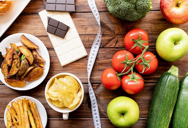 Concepto de comida sana y saludable. Frutas y verduras vs dulces y papas fritas vista superior plana en mesa de madera