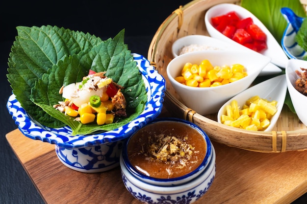 Concepto de comida tailandesa Fusión merienda tailandesa Miang kham a base de hierbas y atún envoltura de un bocado de perilla leafhiso con mezcla de hierbas salsa de azúcar de coco sobre fondo negro con espacio para copiar