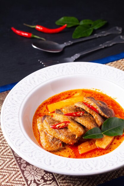 Concepto de comida tailandesa Leche de coco tailandesa pato al curry rojo en plato hondo de cerámica blanca con hierbas estilo tailandés de fondo y espacio de copia