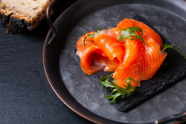 Concepto de comida trucha ahumada o rebanadas de pescado Salmom en tablero de piedra pizarra negra con espacio de copia