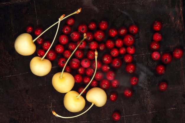 Concepto de comida vegetariana Grosellas rojas jugosas dulces y cerezas amarillas sobre un fondo oscuro Vista desde arriba