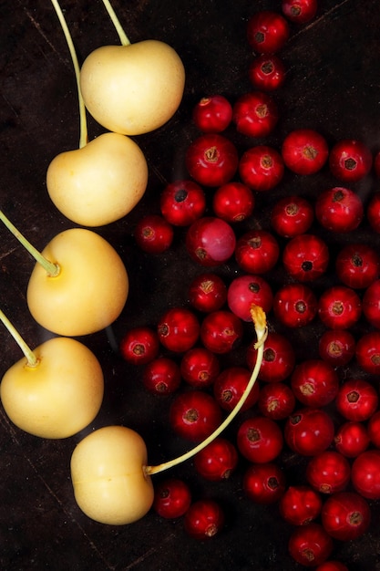 Concepto de comida vegetariana Grosellas rojas jugosas dulces y cerezas amarillas sobre un fondo oscuro Vista desde arriba