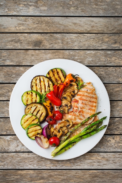 Foto concepto de comida de verano estacional. verduras asadas y pechuga de pollo en un plato sobre una mesa de madera. fondo de espacio de copia plana laicos vista superior