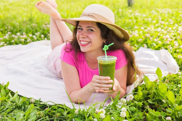 Concepto de comida, verano y personas saludables: la mujer joven se divierte en el parque y bebe batidos verdes en un picnic