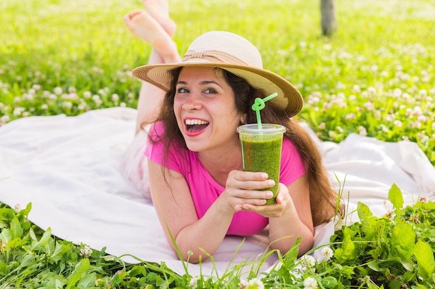 Concepto de comida, verano y personas saludables: la mujer joven se divierte en el parque y bebe batidos verdes en un picnic